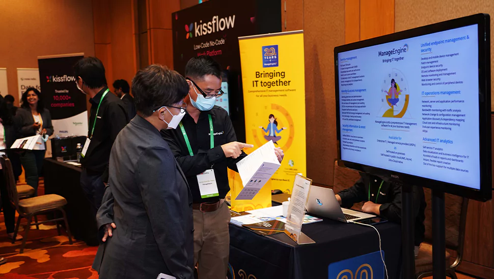 Participants discussing cybersecurity solutions at a vendor booth during the Exito Cybersecurity Summit exhibition area.