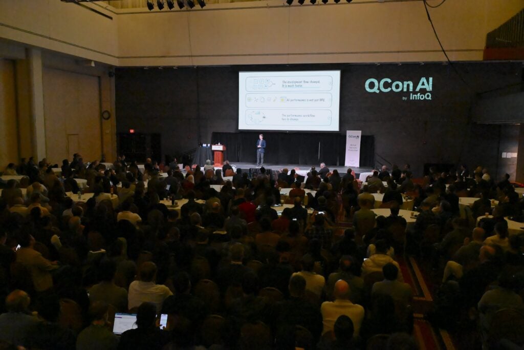 Speaker presenting an AI-focused keynote to a large audience at QCon