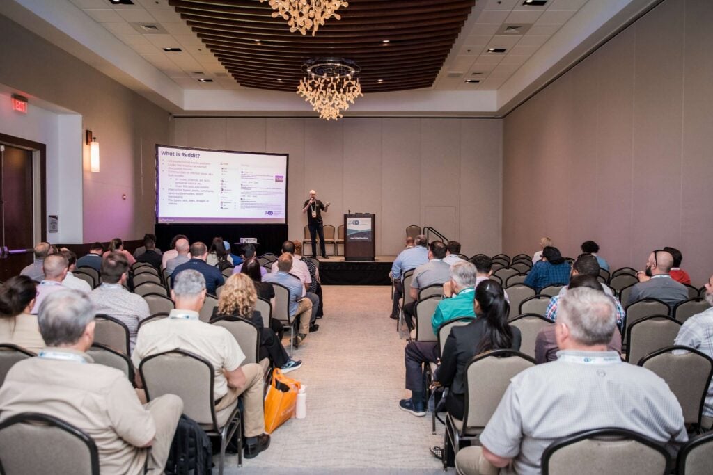Conference participants seated in a session room watching a speaker present on stage at the Techno Security &amp; Digital Forensics Conference.