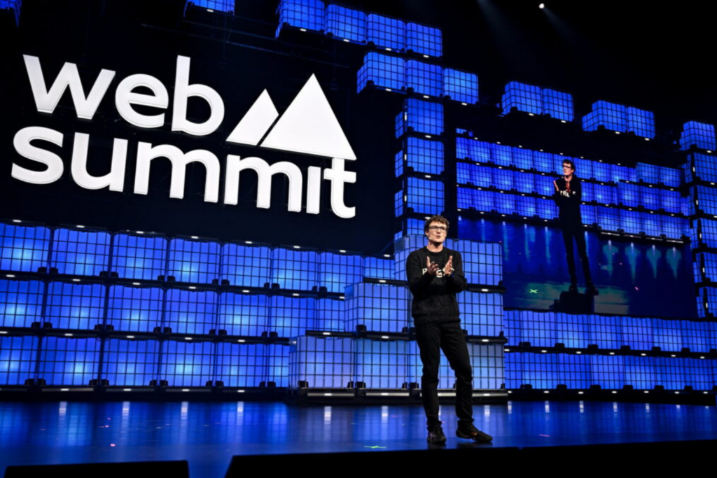 Un ponente principal de pie en el escenario frente a una pantalla grande en Web Summit