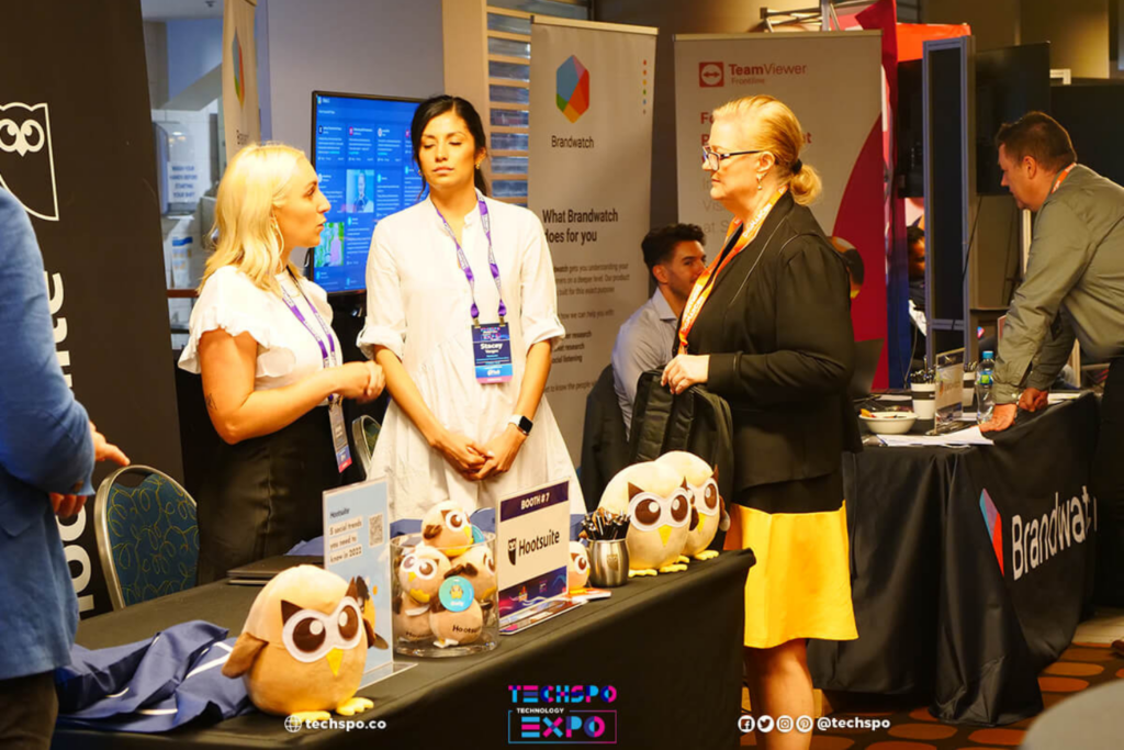 Conference attendees speaking with exhibitors at a booth during TECHSPO Technology Expo